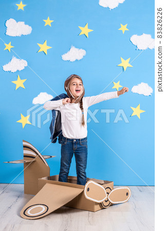 Little dreamer girl playing with a cardboard airplane at the studio with blue sky and white clouds background. Little dreamer girl playing with a cardboard airplane at the studio with blue sky and white clouds background. 83826226