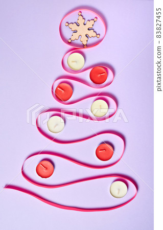 Christmas tree made of pink ribbon on purple paper background decorated with candles and Snowflake on the top of the tree Christmas tree made of pink ribbon on purple paper background decorated with candles and Snowflake on the top of the tree 83827455