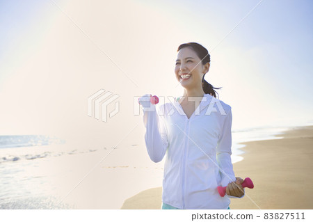 一個穿著運動服的年輕女子在沙灘上散步 83827511