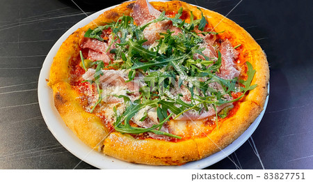 Close-up on a restaurant table pizza with prosciutto, arugula and parmesan cheese Close-up on a restaurant table pizza with prosciutto, arugula and parmesan cheese 83827751