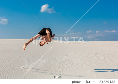 Portrait of young parkour man doing flip or somersault on the sand. 83829488