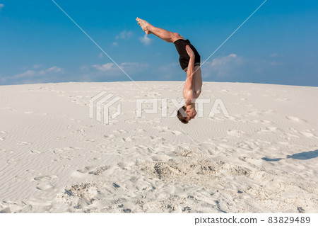 Portrait of young parkour man doing flip or somersault on the sand. Portrait of young parkour man doing flip or somersault on the sand. 83829489