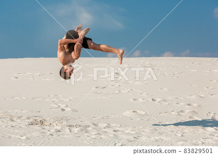 Portrait of young parkour man doing flip or somersault on the sand. Portrait of young parkour man doing flip or somersault on the sand. 83829501