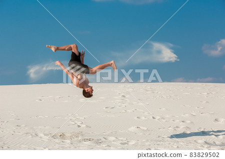 Portrait of young parkour man doing flip or somersault on the sand. Portrait of young parkour man doing flip or somersault on the sand. 83829502