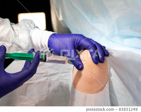 The doctor makes a therapeutic intra-articular injection into the knee joint to relieve inflammation and pain. Therapeutic injections for the restoration of knee cartilage, plasma therapy 83831249