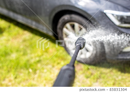 Washing a gray modern car with a manual pressure washer in a summer cottage. Car shampoo for cleaning dirt, transport 83831304