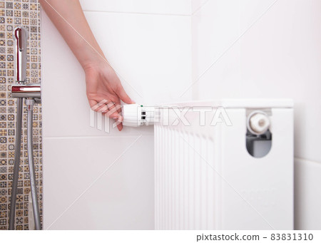 the woman turns on the heating radiator in the bathroom with a thermostat. Setting a comfortable temperature in the bathroom, copy space for text 83831310