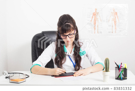 Girl doctor with a graphics tablet on the table in a medical office. Use of graphic tablets in medicine, background 83831332