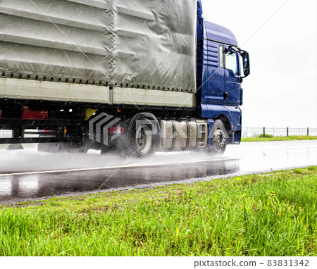 Semi-trailer semitrailer transports cargo on a wet road from rain in summer, close-up. Slippery road, trucking industry Semi-trailer semitrailer transports cargo on a wet road from rain in summer, close-up. Slippery road, trucking industry 83831342