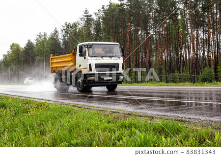 A modern dump truck for transporting bulk cargo drives on the highway in rainy weather. Safe driving in bad weather conditions. Copy space for text, outdoors A modern dump truck for transporting bulk cargo drives on the highway in rainy weather. Safe driving in bad weather conditions. Copy space for text, outdoors 83831343