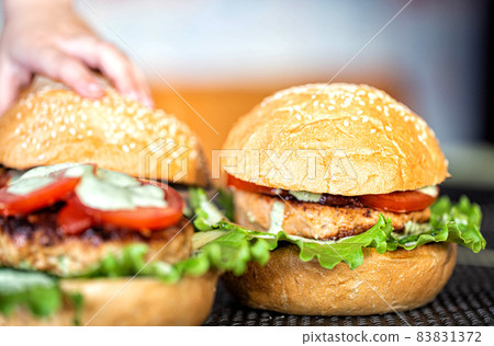 Cooking delicious homemade burgers with cutlet, salad, tomato and sesame burger bun, close-up. Delicious homemade food, fast food, cheeseburger 83831372