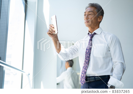 Middle-aged businessman looking at a smartphone in the living room Middle-aged businessman looking at a smartphone in the living room 83837265