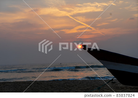 View of sunset with orange clouds. A fishing boat parked on the beach. View of sunset with orange clouds. A fishing boat parked on the beach. 83837824