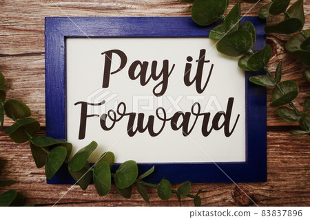 Pay it Forward written on blue frame with green leave flat lay on wooden background 83837896