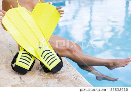 Female hands holding flippers near swimming pool. Concept of summer holidays. Female hands holding flippers near swimming pool. Concept of summer holidays. 83838416