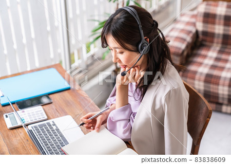 A woman wearing a headset, holding a writing instrument and facing a laptop A woman wearing a headset, holding a writing instrument and facing a laptop 83838609