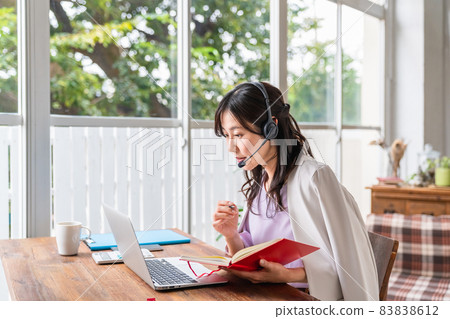 A woman wearing a headset, holding a writing instrument and facing a laptop A woman wearing a headset, holding a writing instrument and facing a laptop 83838612