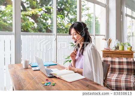 A woman wearing a headset, holding a writing instrument and facing a laptop A woman wearing a headset, holding a writing instrument and facing a laptop 83838613
