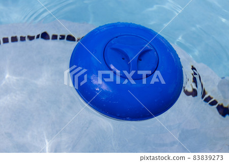 Blue plastic chlorine dispenser floating on the surface of of water in a swimming pool. 83839273