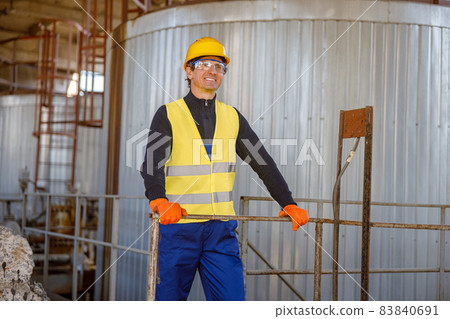 Cheerful man engineer standing near meta storage container at factory Cheerful man engineer standing near meta storage container at factory 83840691