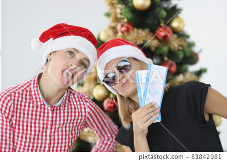 Women in santa hats holding plane tickets near New Year tree 83842981