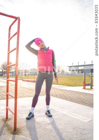 Young fit woman in warm clothes stretches her neck on sports ground outdoors 83843035