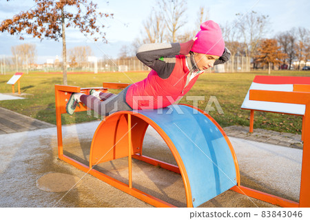 Young athletic fit woman trains her back on workout machine outdoors Young athletic fit woman trains her back on workout machine outdoors 83843046
