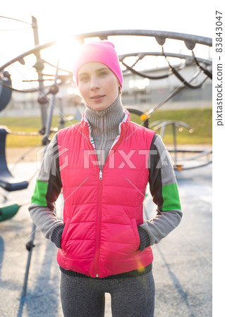 Young fit woman in fitness wear standing on athletic field outdoors on sunrise Young fit woman in fitness wear standing on athletic field outdoors on sunrise 83843047