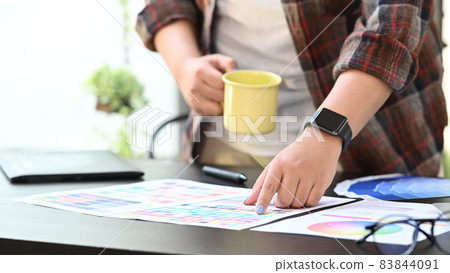 Cropped shot graphic designer holding coffee cup and working with color swatch. 83844091