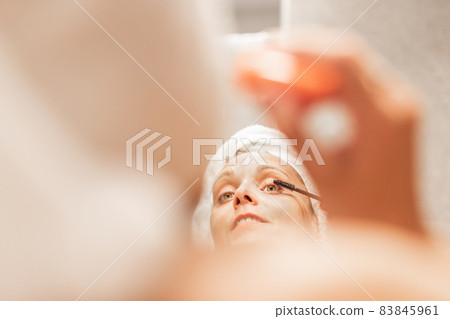 Adult woman applying mascara on eyelash in bathroom. 83845961