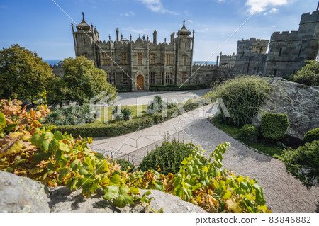 Vorontsov Palace in Alupka, Crimea. Panoramic view of castle with blue sky background. Grape vine with yellow autumnal leaves in foreground 83846882
