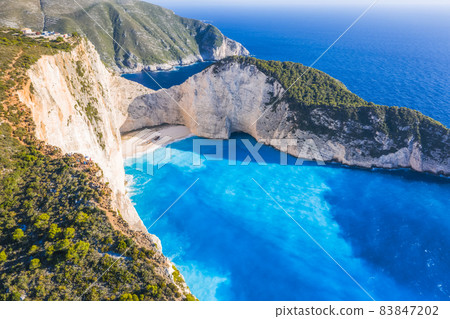 Aerial view of Navagio Beach - Shipwreck beach - on Zakynthos Island, Greece. Tourists on cliff edge enjoy view on summer travel trip Aerial view of Navagio Beach - Shipwreck beach - on Zakynthos Island, Greece. Tourists on cliff edge enjoy view on summer travel trip 83847202