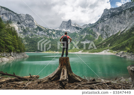 Man traveler standing on tree stump ejoying view of Dachstein peak mountains on a Upper Gosau Lake. Gosau, Salzkammergut, Austria, Europe 83847449
