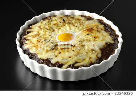 Photographed a grilled curry with plenty of melting cheese and eggs on a black background Photographed a grilled curry with plenty of melting cheese and eggs on a black background 83849320