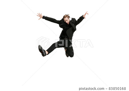 Excited young man in black business suit dancing and listening music isolated on white background. Art, motion, action 83850168