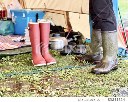 The feet of a man in boots standing in front of a tent on a rainy day 83851814
