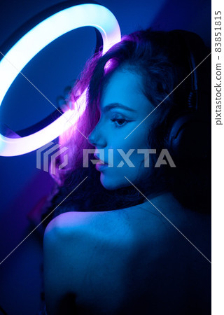 Emotional studio portrait young woman in a wireless headphones with ring flash effect. Round LED Circle Lamp. Emotional studio portrait young woman in a wireless headphones with ring flash effect. Round LED Circle Lamp. 83851815