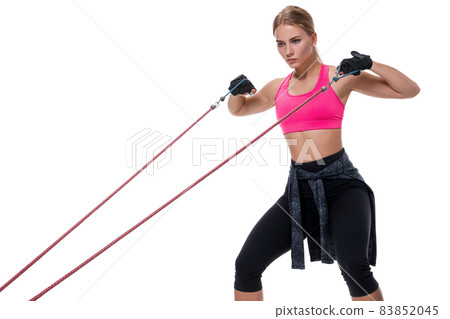 Strong woman using a resistance band in her exercise routine. Young woman performs fitness exercises on white background. Strong woman using a resistance band in her exercise routine. Young woman performs fitness exercises on white background. 83852045