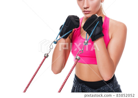 Strong woman using a resistance band in her exercise routine. Young woman performs fitness exercises on white background. Close up Strong woman using a resistance band in her exercise routine. Young woman performs fitness exercises on white background. Close up 83852052