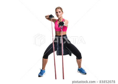 Strong woman using a resistance band in her exercise routine. Young woman performs fitness exercises on white background. 83852078