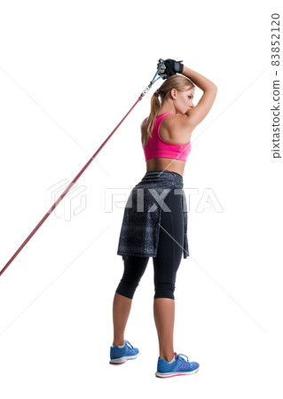 Strong woman using a resistance band in her exercise routine. Young woman performs fitness exercises on white background. Strong woman using a resistance band in her exercise routine. Young woman performs fitness exercises on white background. 83852120