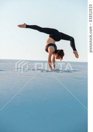 Young woman practicing inversion balancing yoga pose handstand on sand. 83852810