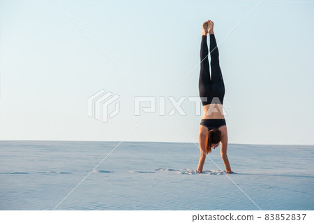Young woman practicing inversion balancing yoga pose handstand on sand. Young woman practicing inversion balancing yoga pose handstand on sand. 83852837