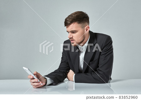 Handsome young man talking on the mobile phone while sitting at his working place in office 83852960