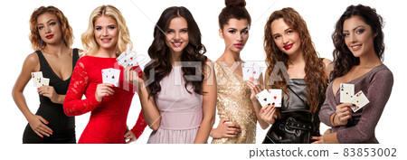 Ladies with make-up and stylish hairstyles, in colorful dresses and jewelry. Smiling, showing aces, posing isolated on white. Poker, casino. Close-up Ladies with make-up and stylish hairstyles, in colorful dresses and jewelry. Smiling, showing aces, posing isolated on white. Poker, casino. Close-up 83853002