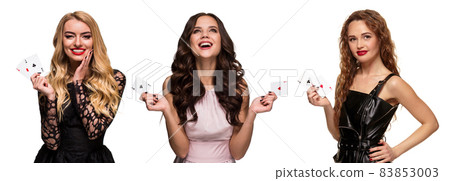 Three girls with make-up and hairstyles, in pink and black dresses, jewelry. Smiling, showing aces, posing isolated on white. Poker, casino. Close-up Three girls with make-up and hairstyles, in pink and black dresses, jewelry. Smiling, showing aces, posing isolated on white. Poker, casino. Close-up 83853003