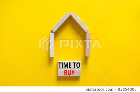 Time to buy house symbol. Concept words 'Time to buy' on wooden blocks near miniature house. Beautiful yellow background, copy space. Business and time to buy house concept. 83854003