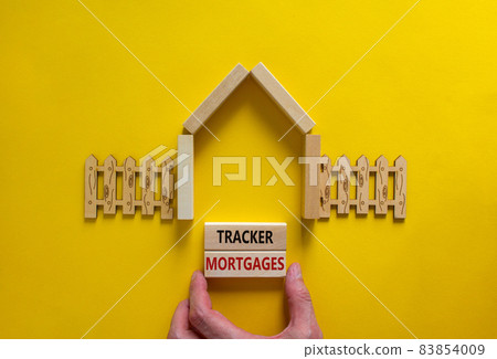 Tracker mortgage symbol. Concept words 'Tracker mortgage' on wooden blocks on a beautiful yellow backgrounds. Businessman hand. House model and wooden fence. Business, tracker mortgage concept. 83854009