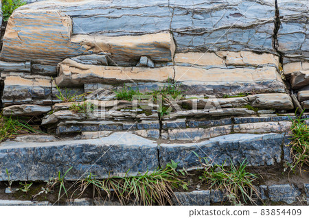 Layered wild stone close-up sandstone rock protruding from ground Layered wild stone close-up sandstone rock protruding from ground 83854409