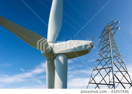Wind Turbine and High Voltage Tower against a Blue Sky - Renewable Energy 83855486